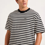 A man wearing a black and white horizontally striped t-shirt with a black crew neck collar, shown from the chest up against a light gray studio background.