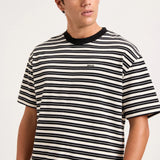A man wearing a black and white horizontally striped t-shirt with a black crew neck collar, shown from the chest up against a light gray studio background.