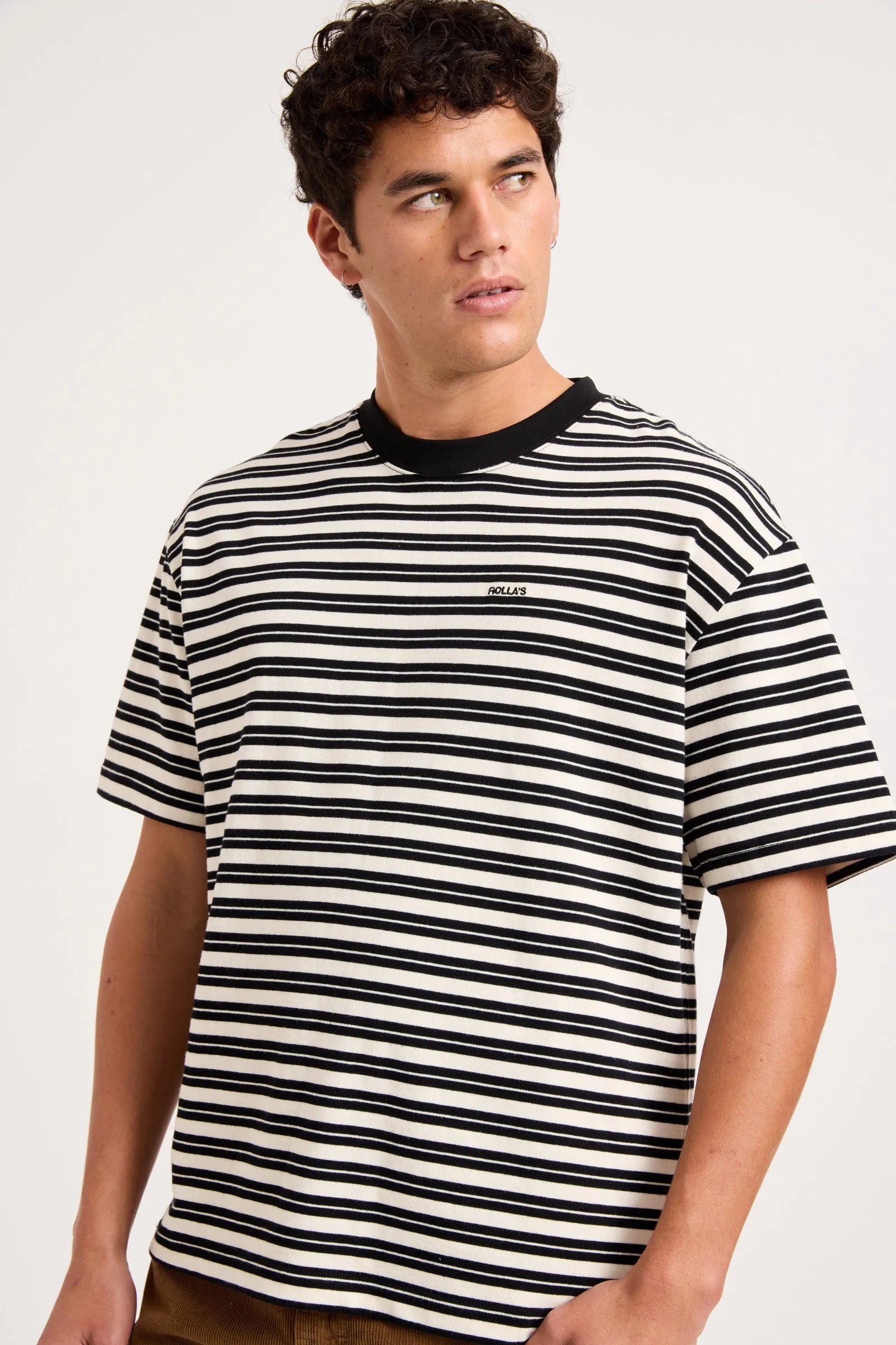 A man wearing a black and white horizontally striped t-shirt with a black crew neck collar, shown from the chest up against a light gray studio background.