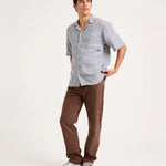 A man modeling a light gray short-sleeve button-up shirt with a subtle micro-check pattern, paired with brown corduroy pants and gray sneakers, against a plain white studio background.