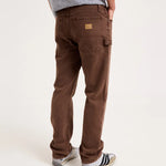 A person shown from the back wearing brown cargo-style pants, a gray patterned t-shirt, and gray sneakers with black stripes, against a plain light background.
