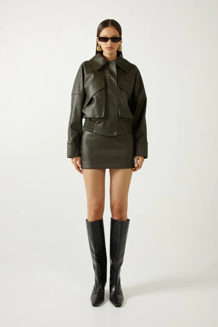Woman wearing a dark green leather jacket, skirt, and boots on a white background