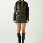 Woman wearing a dark green leather jacket, skirt, and boots on a white background