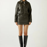 Woman wearing a dark green leather jacket, skirt, and boots on a white background
