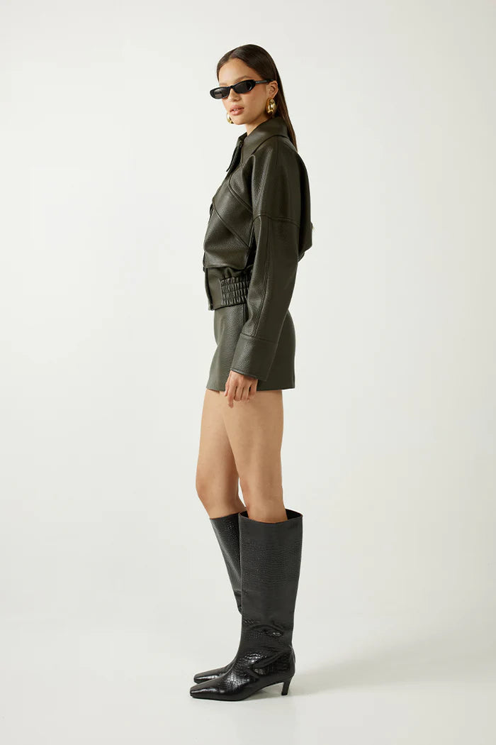 Woman wearing a green leather outfit with black knee-high boots on a white background