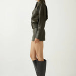Woman wearing a green leather outfit with black knee-high boots on a white background