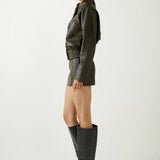 Woman wearing a green leather outfit with black knee-high boots on a white background