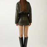 Person wearing a green leather outfit with black boots on a white background