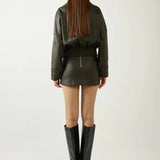 Person wearing a green leather outfit with black boots on a white background
