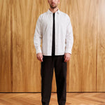 A man stands against a wood-paneled wall wearing a white long-sleeve button-up shirt, a black tie, and black trousers. Text at the bottom reads 'MODEL 18-60 (183CM)' and 'SIZE MEDIUM'.