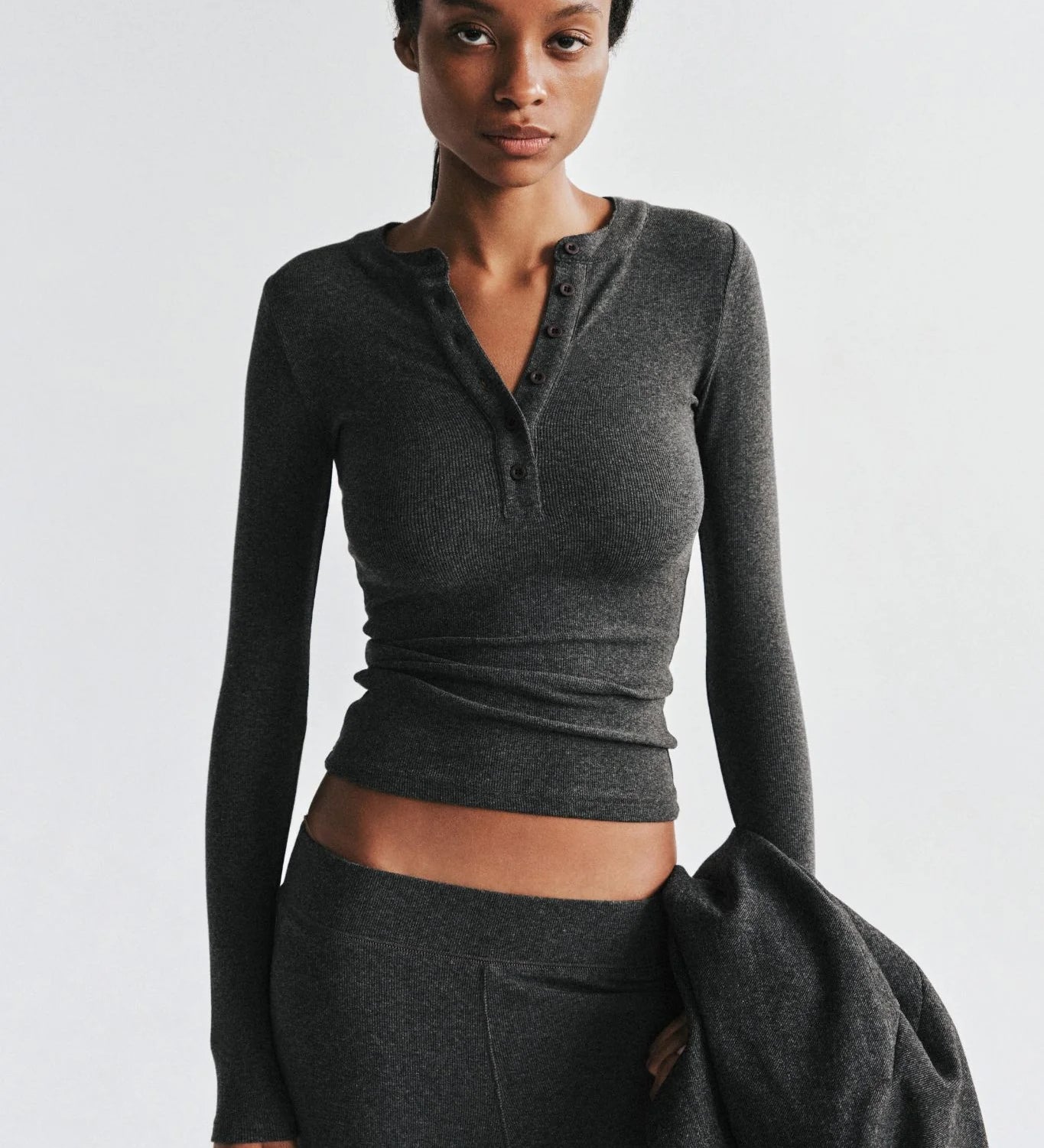 Woman wearing a gray long-sleeve top and pants against a white background