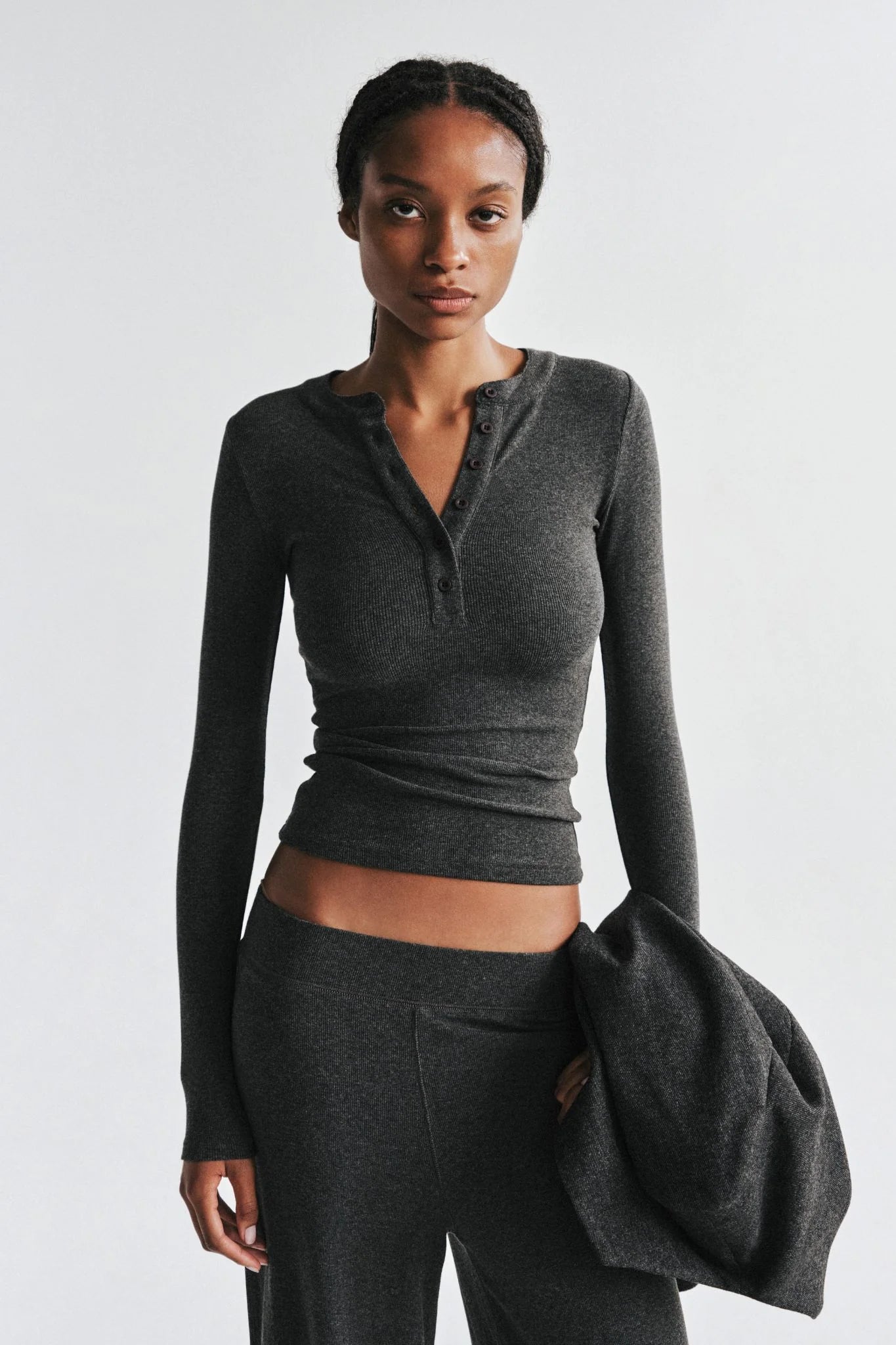 Woman wearing a gray long-sleeve top and pants against a white background