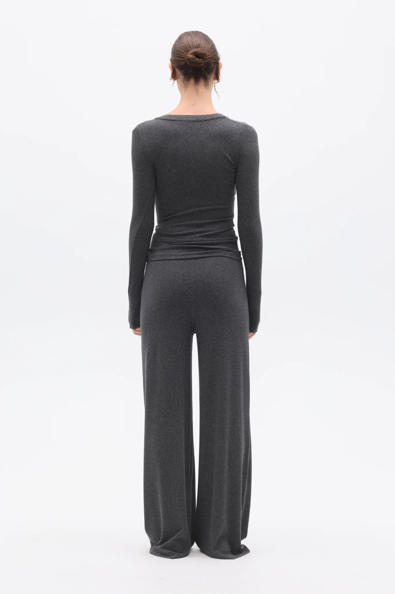 Person wearing a dark gray long-sleeve top and wide-leg pants on a white background