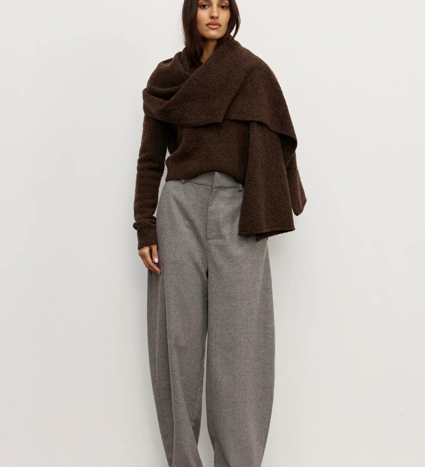 Woman wearing a brown Scarf over a brown sweater and gray pants against a white background