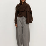 Woman wearing a brown Scarf over a brown sweater and gray pants against a white background