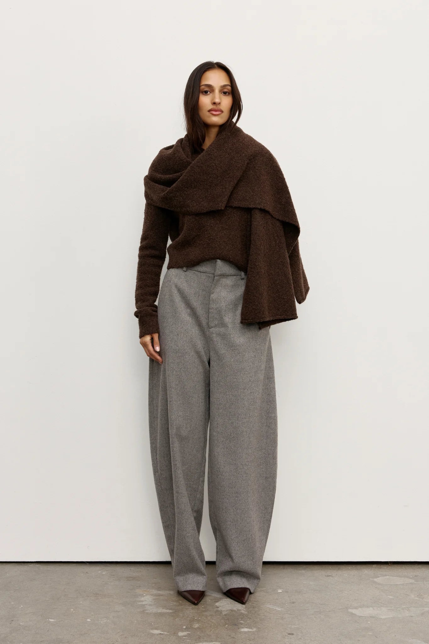 Woman wearing a brown Scarf over a brown sweater and gray pants against a white background
