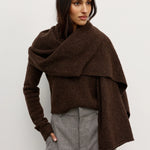 Woman wearing a brown Scarf over a brown sweater and gray pants against a white background