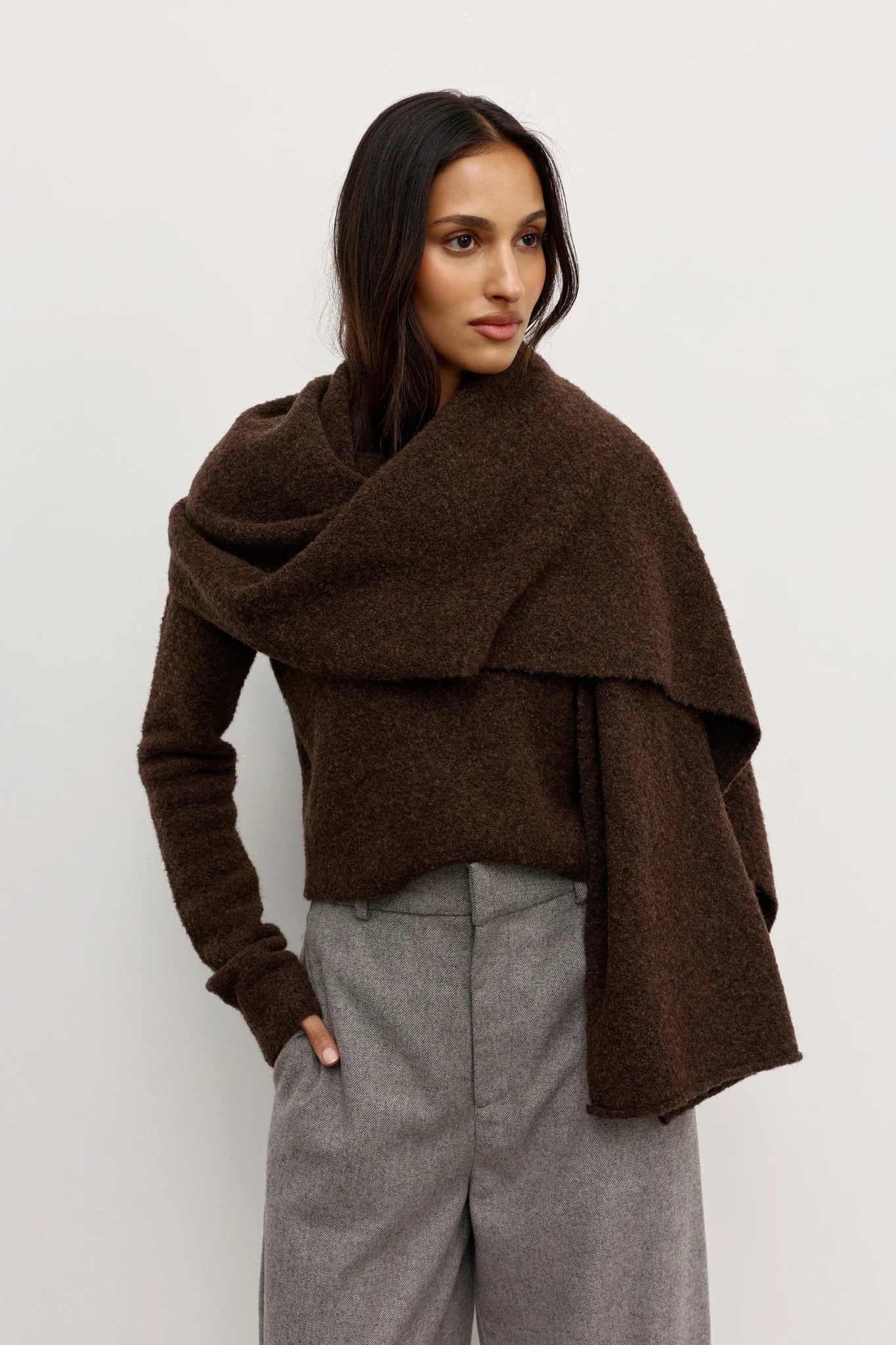 Woman wearing a brown Scarf over a brown sweater and gray pants against a white background