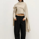 Woman wearing a beige Scarf over a  sweater and black pants against a white background