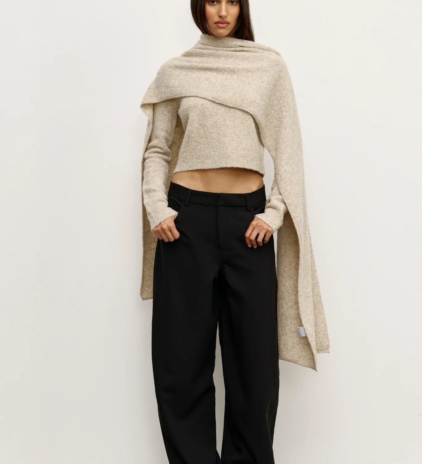 Woman wearing a beige Scarf over a  sweater and black pants against a white background