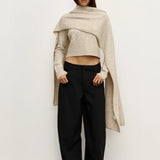 Woman wearing a beige Scarf over a  sweater and black pants against a white background