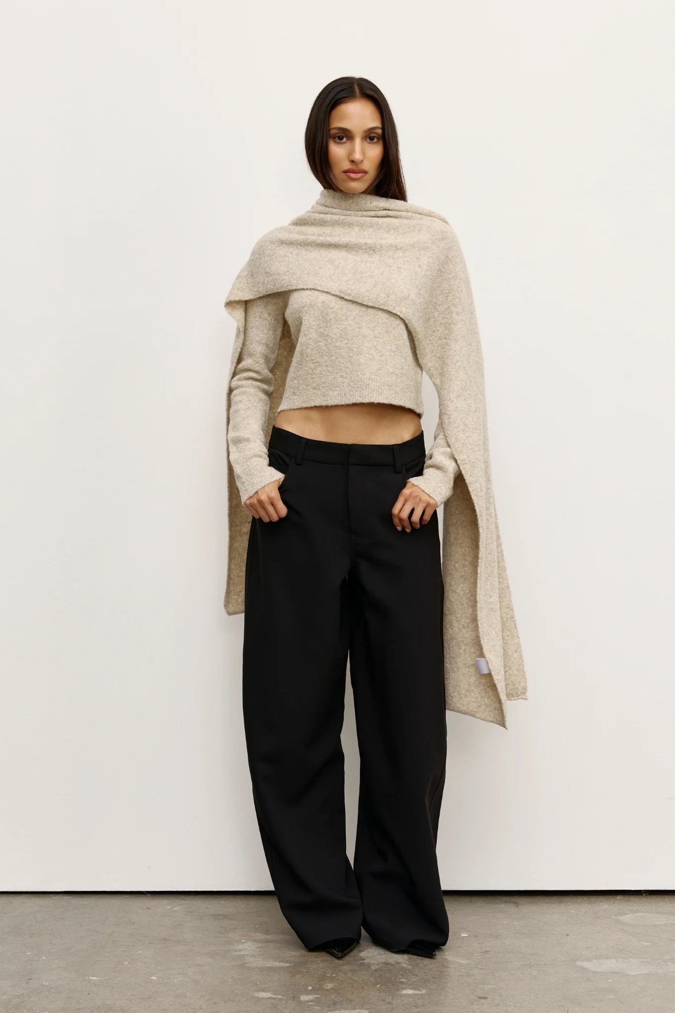 Woman wearing a beige Scarf over a  sweater and black pants against a white background