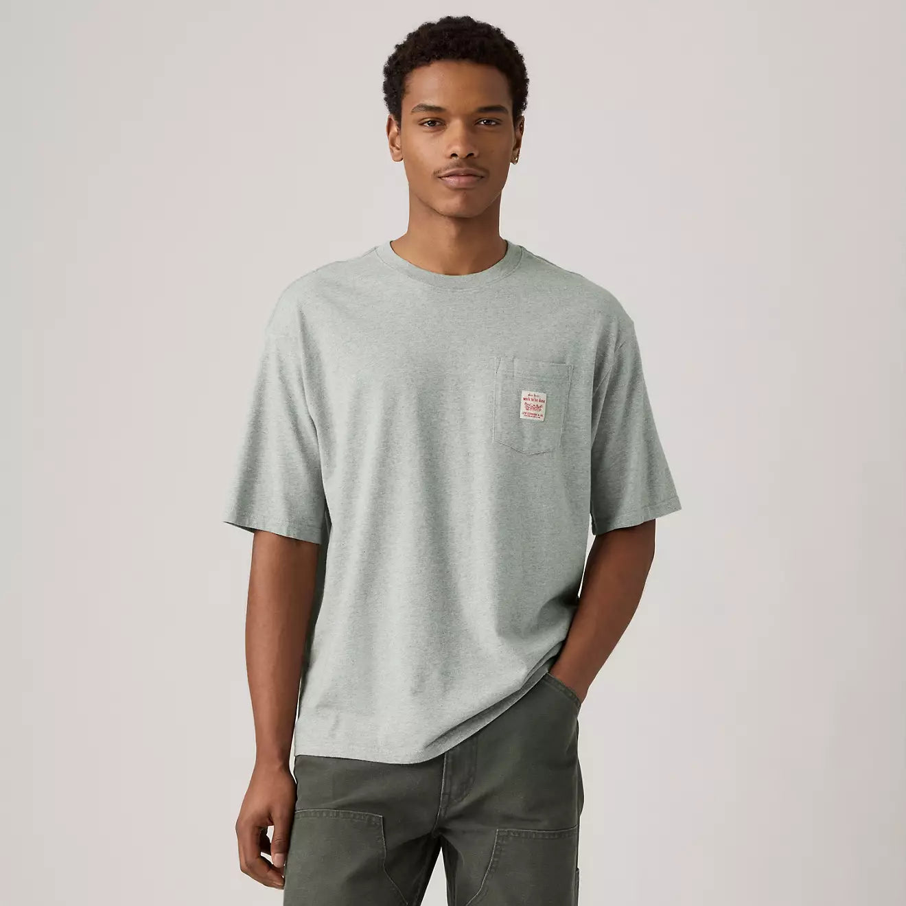 Man wearing a light gray t-shirt with a small logo on a plain background