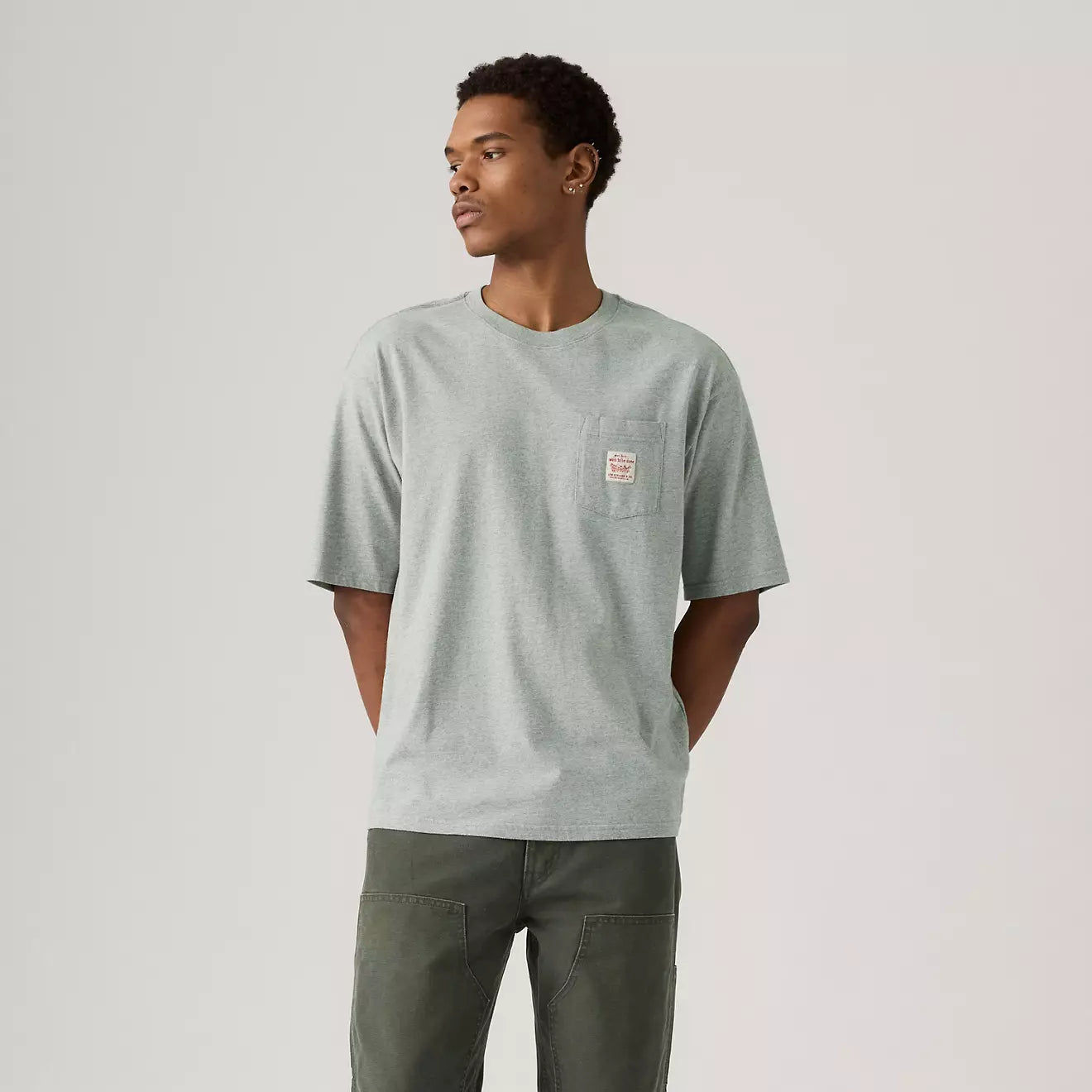 Man wearing a light gray t-shirt with a pocket on a plain background