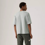 Person wearing a light gray t-shirt and dark green pants on a plain background