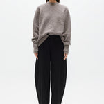 Woman wearing a gray sweater and black pants on a white background