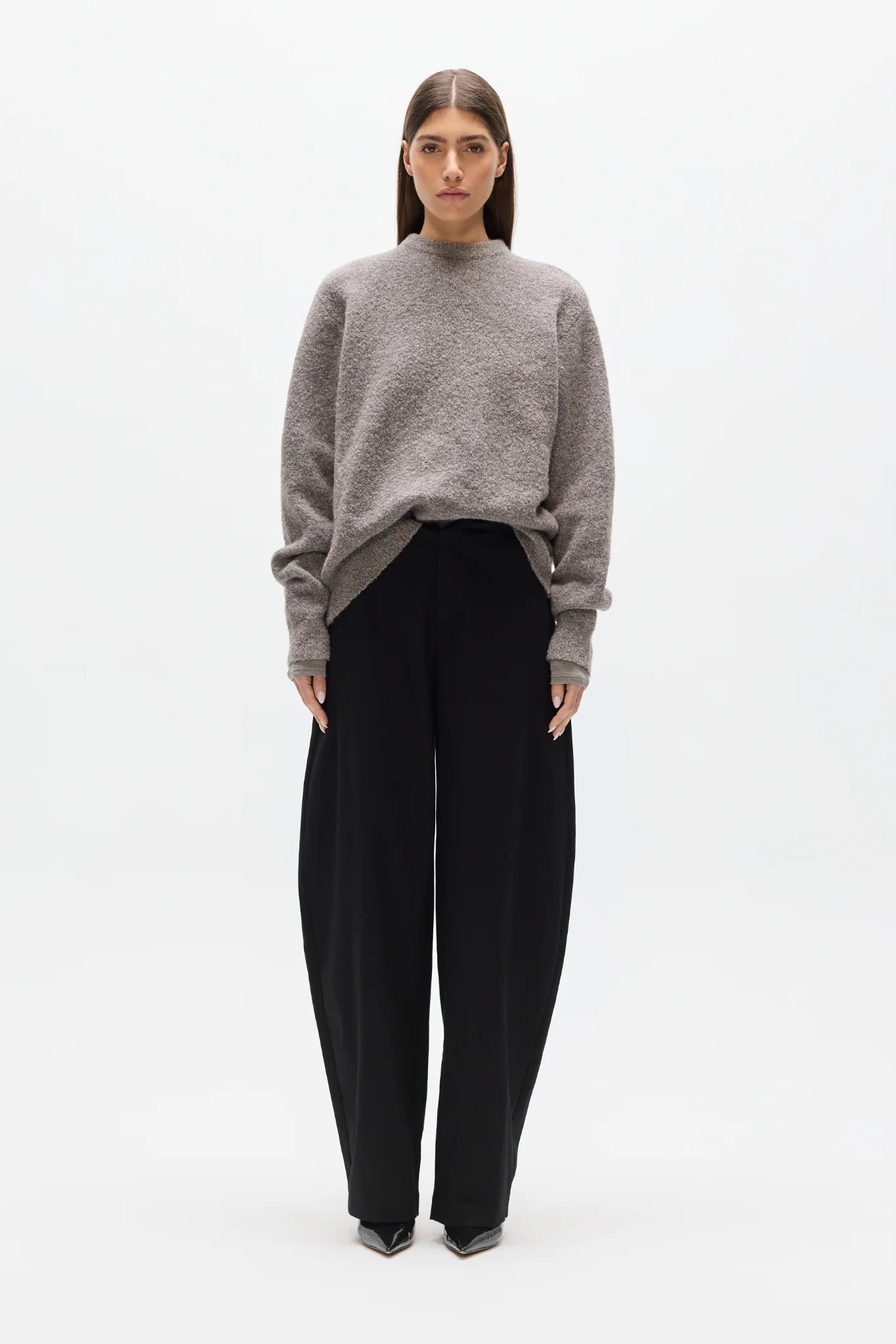 Woman wearing a gray sweater and black pants on a white background