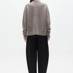 Person wearing a gray sweater and black pants on a white background