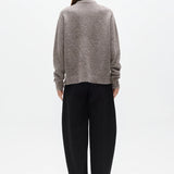 Person wearing a gray sweater and black pants on a white background