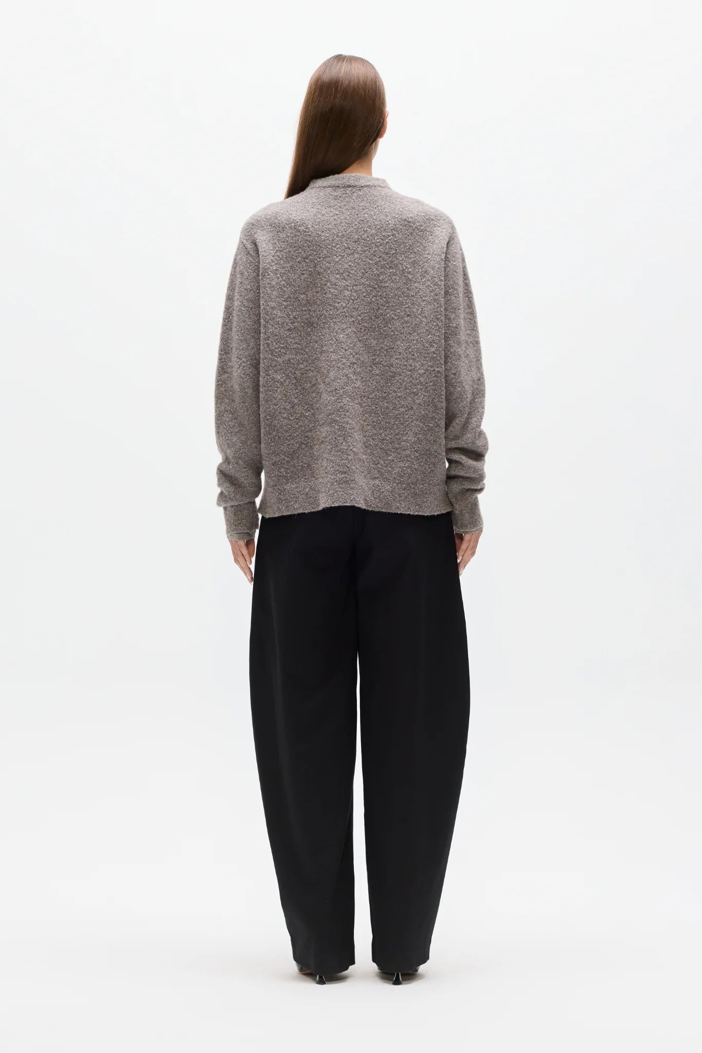Person wearing a gray sweater and black pants on a white background