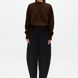 Woman wearing a brown sweater and black pants on a white background