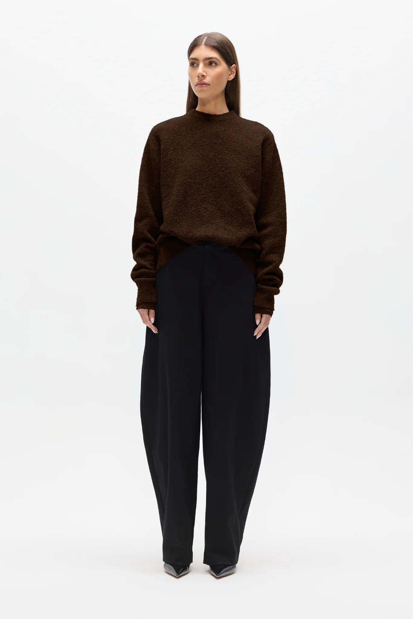 Woman wearing a brown sweater and black pants on a white background