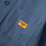 Close-up of a blue shirt with a yellow label on the chest pocket.
