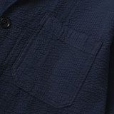 Close-up of a textured navy blue jacket with a pocket and button detail.