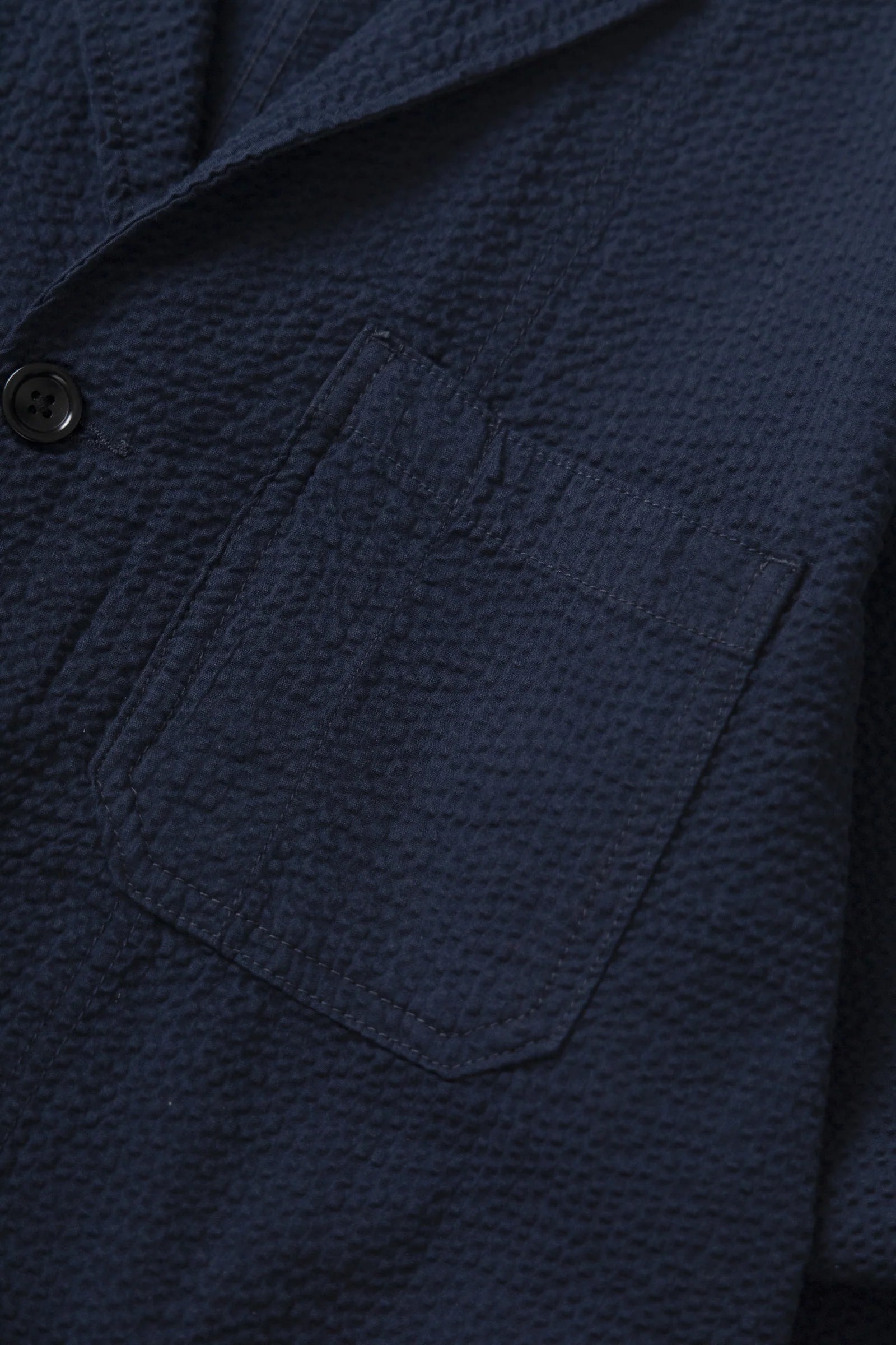 Close-up of a textured navy blue jacket with a pocket and button detail.