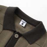 Close-up of a brown polo shirt with a black collar and button, featuring a brand label on a white background.