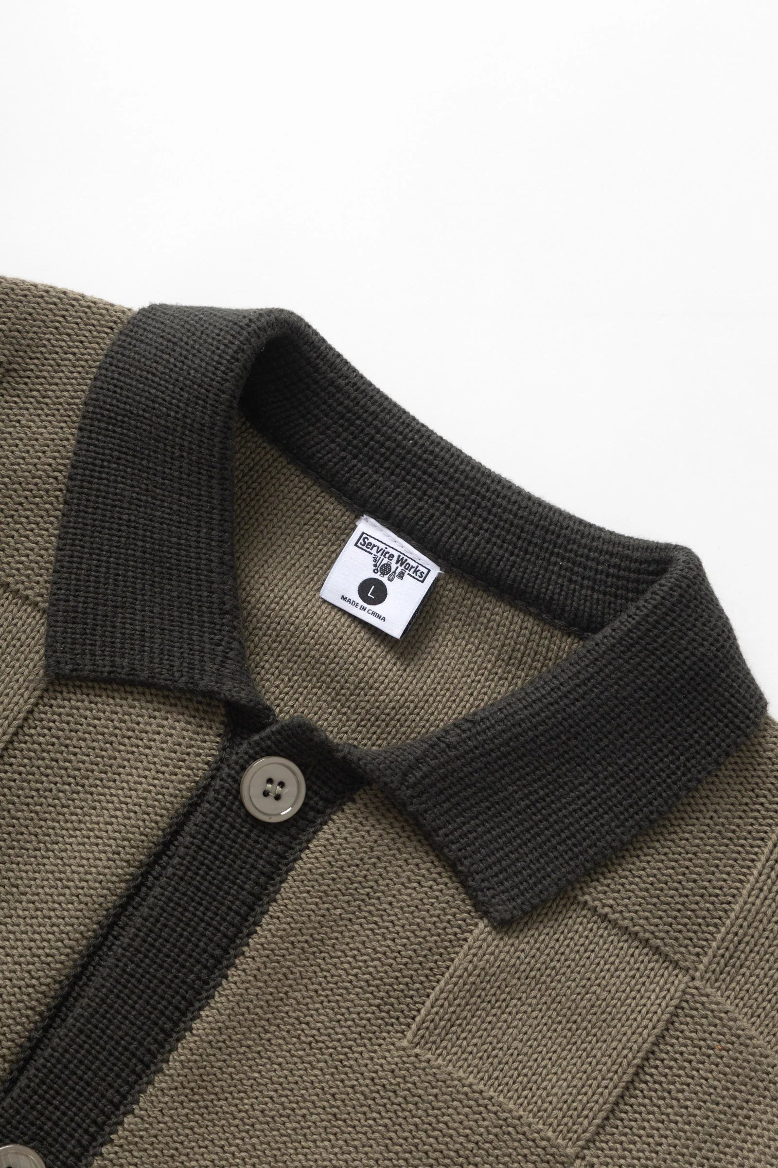 Close-up of a brown polo shirt with a black collar and button, featuring a brand label on a white background.