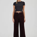 Woman wearing a black t-shirt and dark brown wide-leg pants on a white background