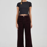 Woman wearing a black t-shirt and dark brown wide-leg pants on a white background