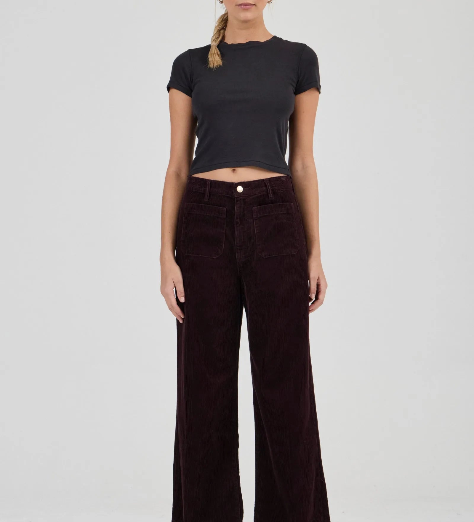 Woman wearing a black t-shirt and dark brown wide-leg pants on a white background