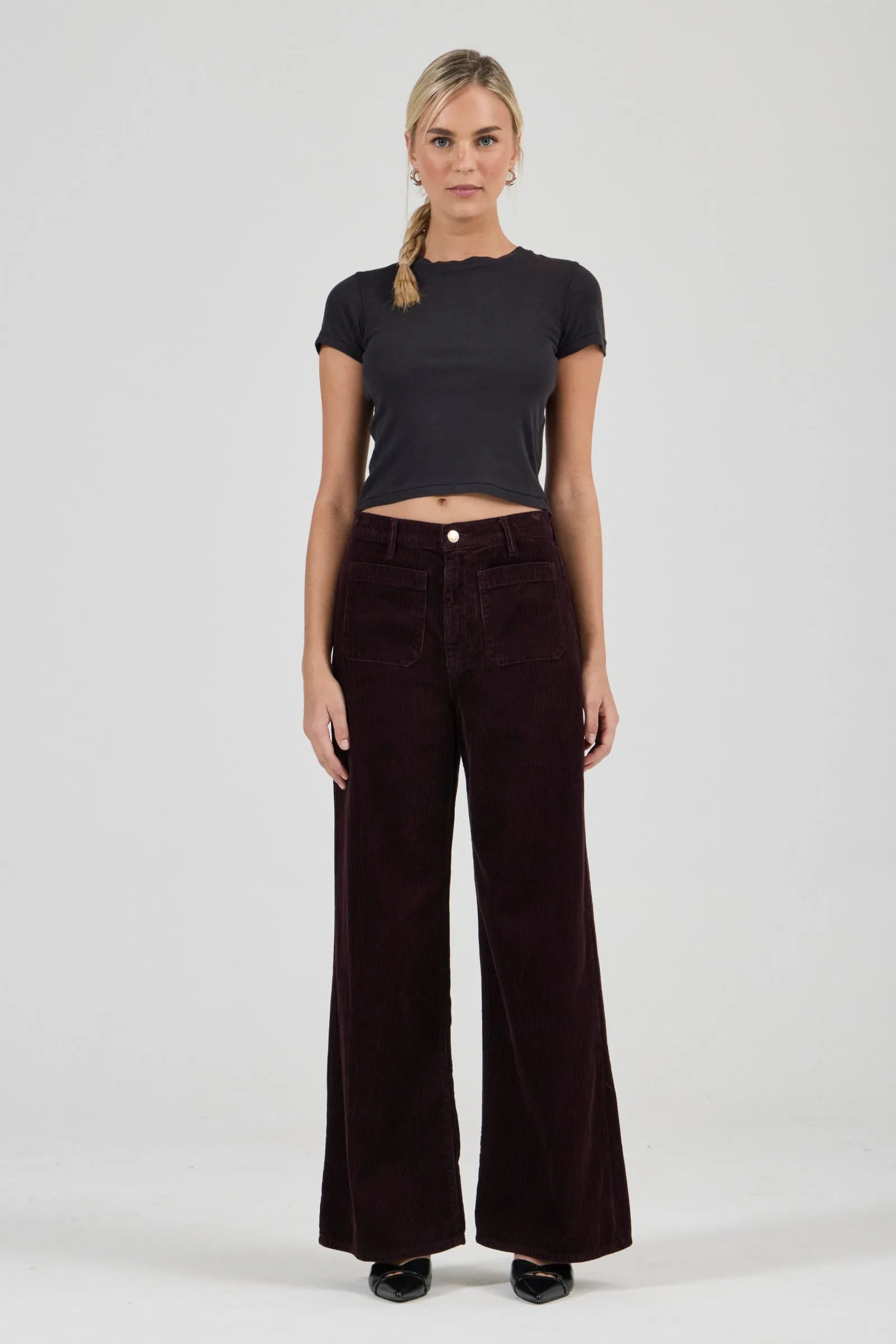 Woman wearing a black t-shirt and dark brown wide-leg pants on a white background