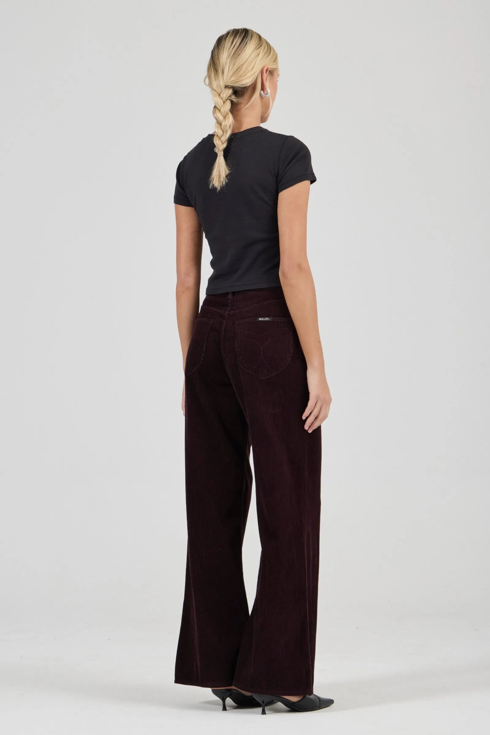 Woman wearing a black t-shirt and dark brown pants on a white background