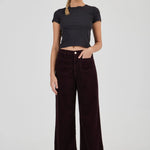 Woman wearing a black t-shirt and dark brown wide-leg pants on a white background