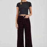 Woman wearing a black t-shirt and dark brown wide-leg pants on a white background