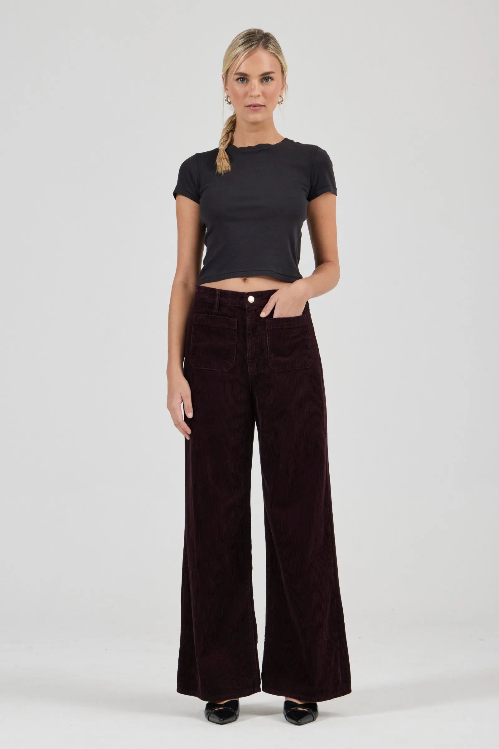 Woman wearing a black t-shirt and dark brown wide-leg pants on a white background