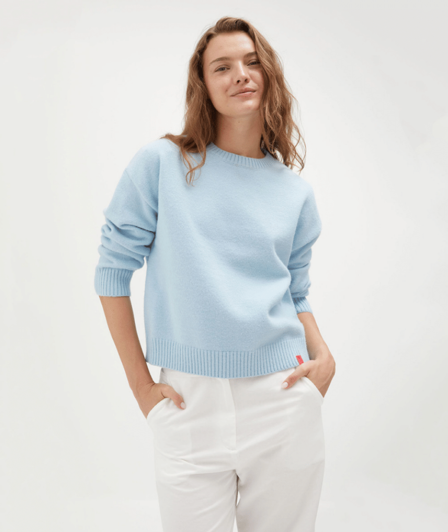 Woman wearing a light blue sweater with three additional sweaters displayed below on a white background.